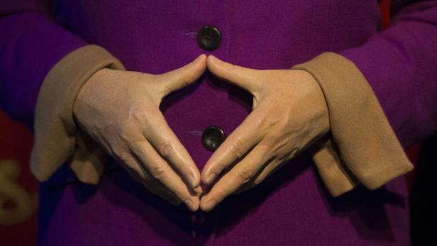 Die Hände einer Person formen eine Raute vor einem violetten Blazer.