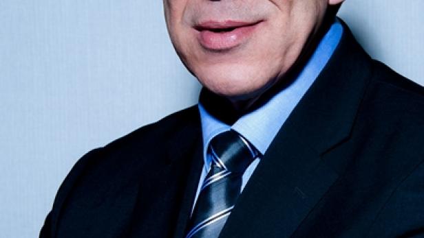Ein Mann mit grauem Haar und Anzug blickt in die Kamera.