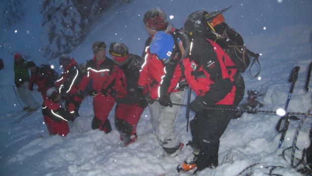 Eine Gruppe von Bergsteigern steigt bei starkem Schneefall einen verschneiten Hang hinauf.