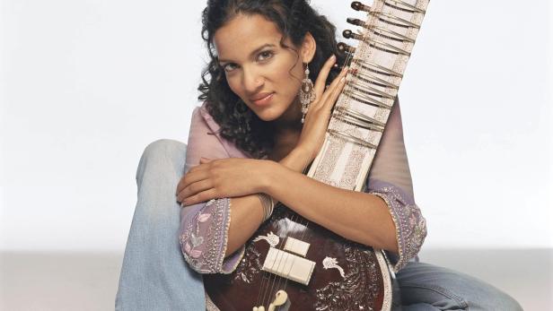 Eine Frau sitzt barfuß da und hält eine Sitar in ihren Armen.