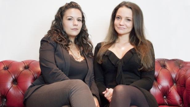 Zwei Frauen sitzen auf einem roten Ledersofa.