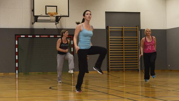 Drei Frauen machen in einer Turnhalle Kniehebelauf.