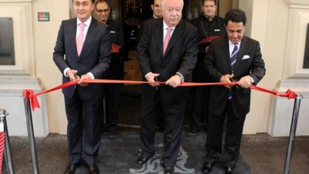 Drei Männer in Anzügen durchschneiden ein rotes Band vor dem Eingang des The Ritz-Carlton Hotels.