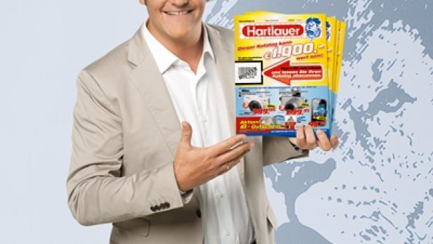 Ein Mann mit Brille präsentiert Kataloge der Firma Hartlauer.