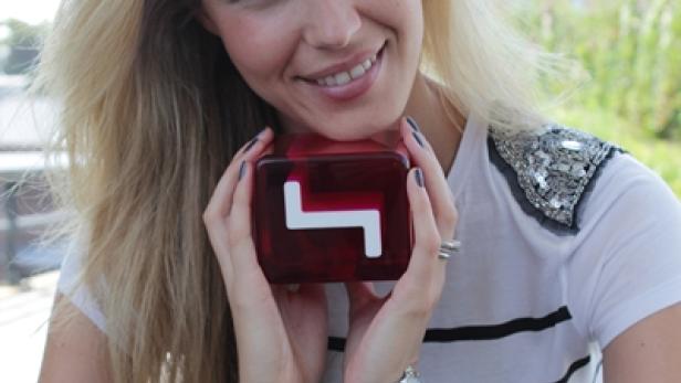 Eine blonde Frau hält einen roten Würfel mit einem weißen L-förmigen Symbol in ihren Händen.