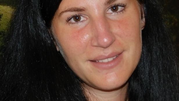 Porträt einer Frau mit langen, dunklen Haaren vor einem Landschaftshintergrund.