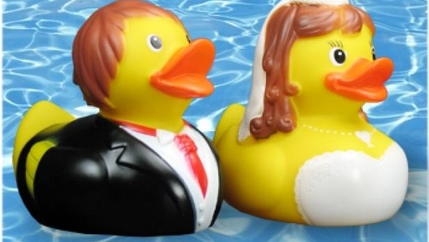 Zwei gelbe Badeenten, als Braut und Bräutigam verkleidet, schwimmen im Wasser.