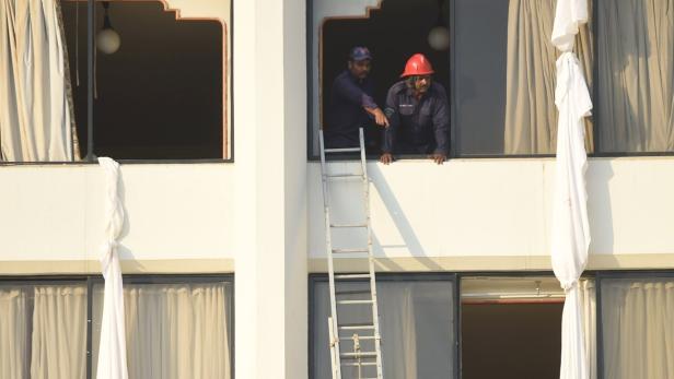 Zwei Männer stehen an einem Fenster, eine Leiter lehnt an der Fassade.