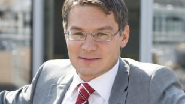 Ein Mann mit Brille und Anzug schaut in die Kamera.