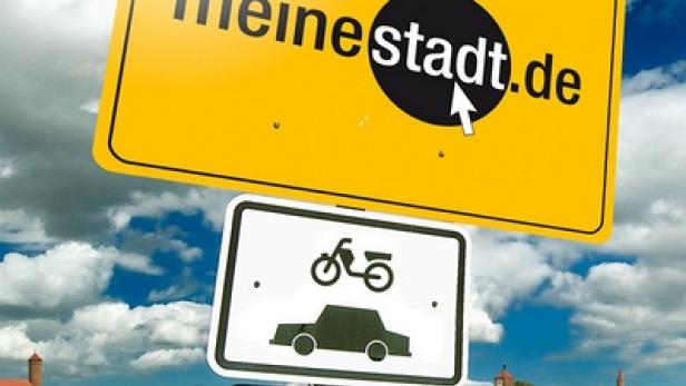 Ein Schild mit der Aufschrift „meine Stadt.de“ vor einem ländlichen Hintergrund mit Verkehrsschildern.