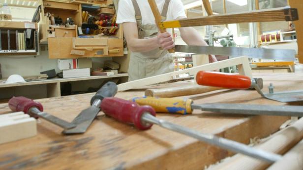 Ein Tischler sägt Holz in seiner Werkstatt, Werkzeuge liegen im Vordergrund.