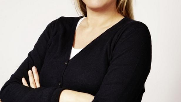 Eine Frau mit blonden Haaren und blauem Pullover mit verschränkten Armen.