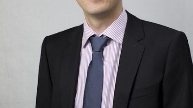 Ein Mann mit Anzug und Krawatte lächelt in die Kamera.