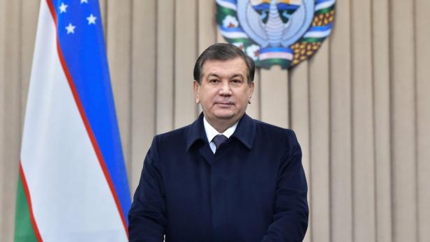 Der Präsident von Usbekistan, Shavkat Mirziyoyev, posiert vor der usbekischen Flagge.