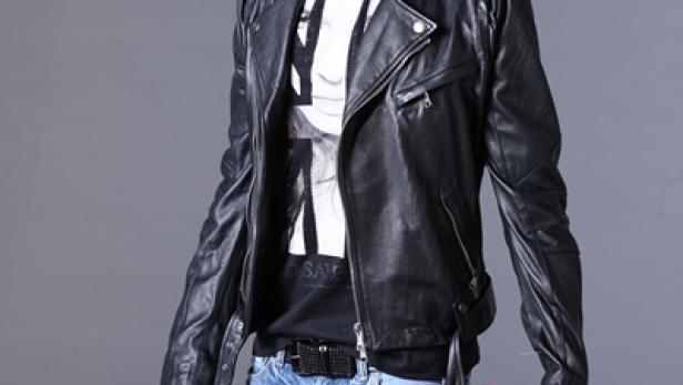 Ein junger Mann mit Lederjacke und Jeans hält einen roten Würfel in der Hand.