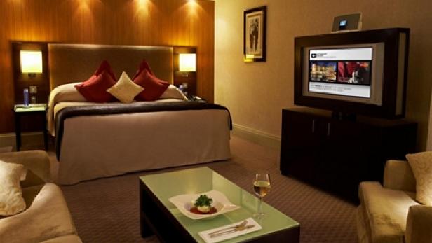 Ein luxuriöses Hotelzimmer mit einem großen Bett, einem Fernseher und einem Couchtisch mit Speisen und Getränken.