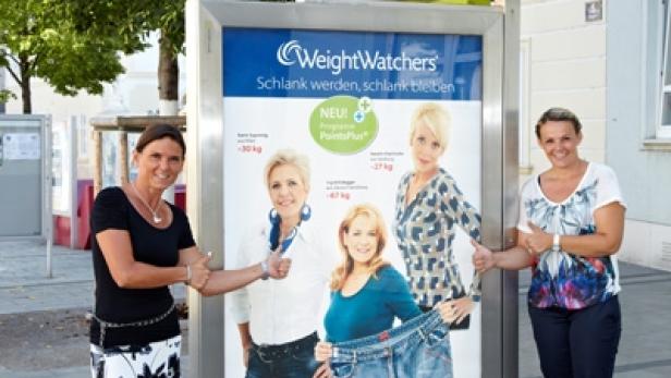 Zwei Frauen geben vor einer Weight Watchers-Werbung an einer Bushaltestelle einen Daumen nach oben.