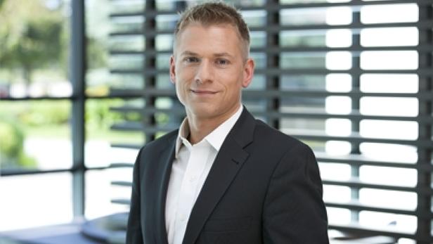 Ein Mann mit blonden Haaren und einem dunklen Anzug lächelt in die Kamera.