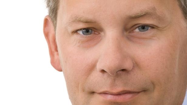 Porträt eines Mannes in Anzug und Hemd vor einem weißen Hintergrund.