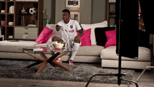Ein junger Mann im Fußballtrikot sitzt mit Popcorn vor dem Fernseher.