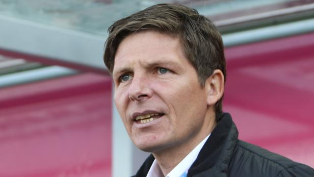 Ein Mann mit hellbraunen Haaren und einer schwarzen Jacke steht vor einem rosa Hintergrund.