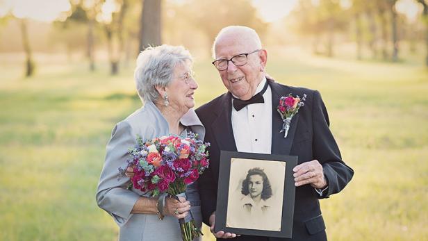 Ein älteres Paar hält ein Hochzeitsfoto der Frau aus jungen Jahren in der Hand.