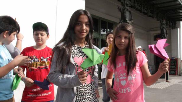 Eine Gruppe von Kindern hält bunte Origami-Figuren in der Hand.