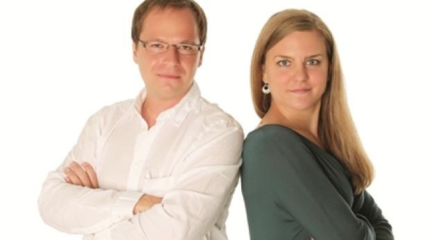 Ein Mann mit Brille und eine Frau stehen Rücken an Rücken vor einem weißen Hintergrund.