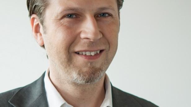 Ein Mann mit Anzug lächelt in die Kamera.