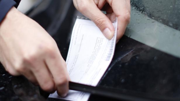 Eine Person befestigt einen Parkschein der Firma „PANTEST“ an der Windschutzscheibe eines Autos.
