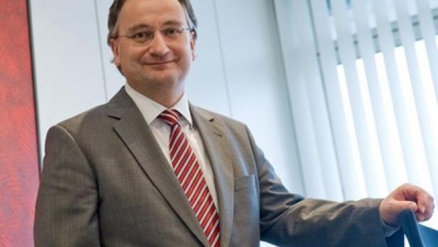 Ein Mann mit Brille und Anzug steht vor einem Fenster.