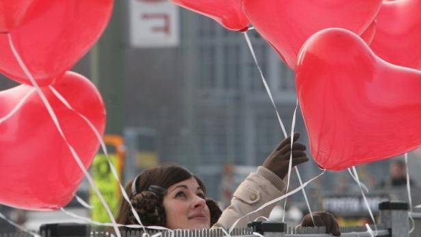 Eine junge Frau knotet am Dienstag (14.02.2012) in Berlin rote Herz-Luftballons zum Valentinstag an einen Zaun. Foto: Stephanie Pilick dpa/lbn +++(c) dpa - Bildfunk+++