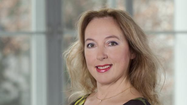 Porträt einer lächelnden Frau mit blonden Haaren und einer goldenen Halskette.