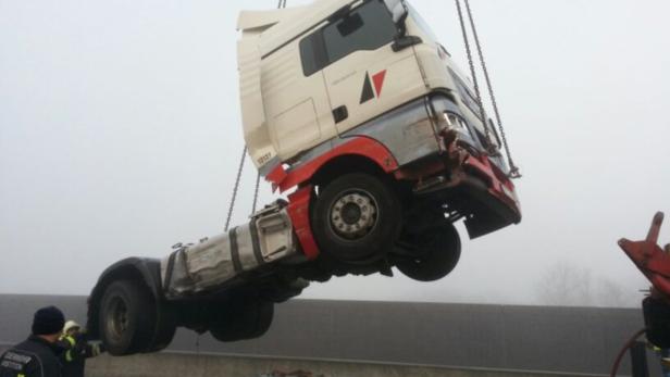 Ein beschädigter LKW wird mit einem Kran auf einen Tieflader gehoben.