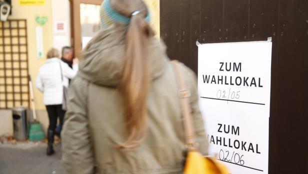 Eine Person geht an einem Wahllokal vorbei, an der Tür hängen Hinweisschilder.