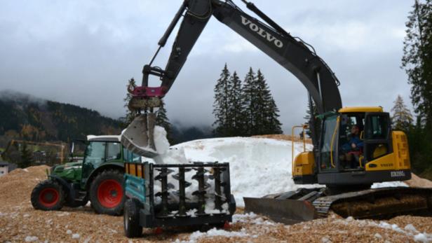 Ein Bagger von Volvo befüllt einen Anhänger mit Schnee neben einem Traktor.