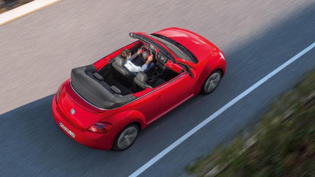 Ein rotes VW Käfer Cabriolet fährt auf einer Straße.