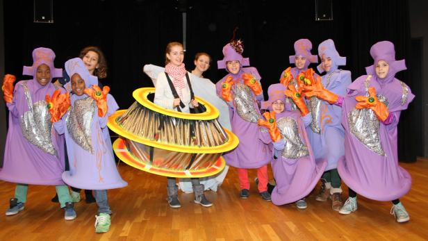 Eine Gruppe Kinder in fantasievollen, lilafarbenen Kostümen steht auf einer Bühne.