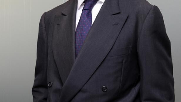 Ein Mann mit Brille und dunklem Anzug posiert für ein Porträt.