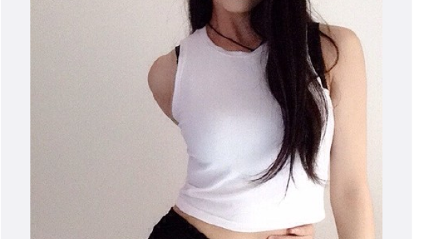 Eine junge Frau posiert in einem weißen Top und einem schwarzen Rock vor einer Wand.