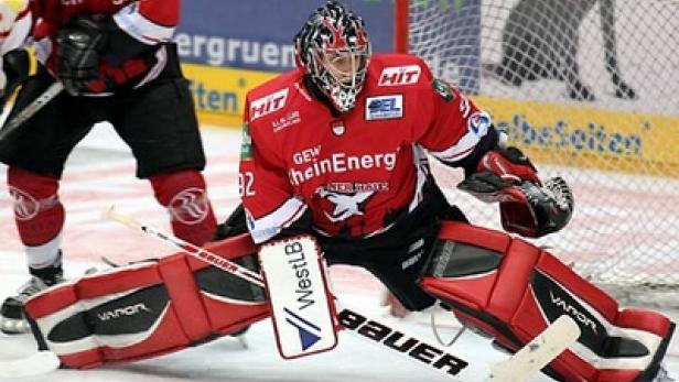 Ein Eishockeytorwart in roter Schutzkleidung steht vor dem Netz.