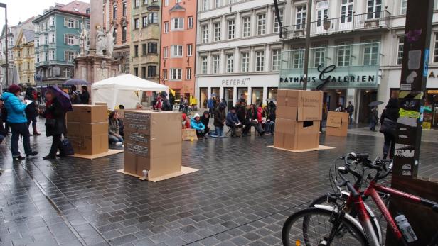 Eine Performance mit beschrifteten Kartons auf einem Platz in Innsbruck.