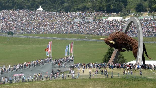 Eine große Menschenmenge versammelt sich vor einer Stier-Skulptur auf einer grünen Wiese.