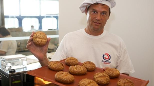 Ein Bäcker präsentiert frisch gebackene Brötchen.