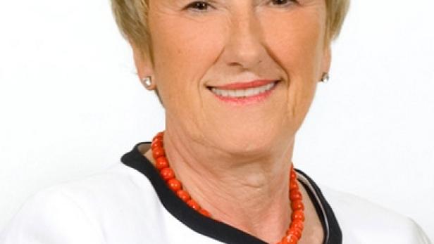Porträt einer lächelnden Frau mit kurzem blonden Haar und einer roten Halskette.