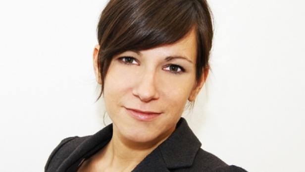 Eine junge Frau mit braunen Haaren und einem Blazer lächelt.