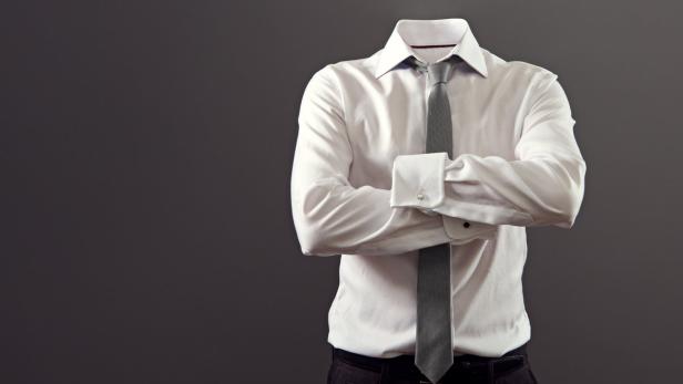 Eine formelle, unsichtbare Person mit verschränkten Armen, Hemd und Krawatte vor grauem Hintergrund.