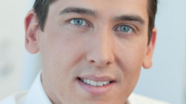 Ein Mann mit hellblauen Augen und einem weißen Hemd lächelt in die Kamera.