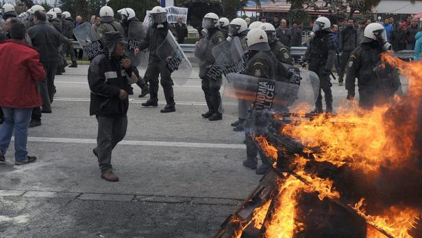 Polizisten in Schutzausrüstung stehen vor einem brennenden Barrikade.