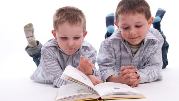 Zwei Jungen liegen auf dem Boden und lesen ein Buch.